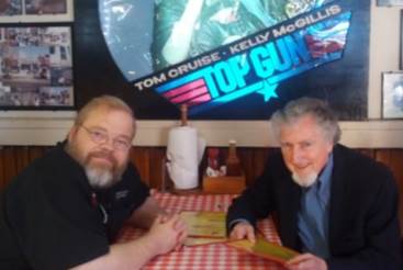 Men sitting at a table with a poster on the wall

AI-generated content may be incorrect.